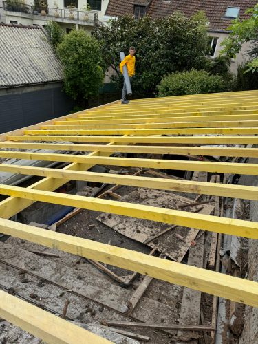 Homme travailleur sur charpente en bois jaune.